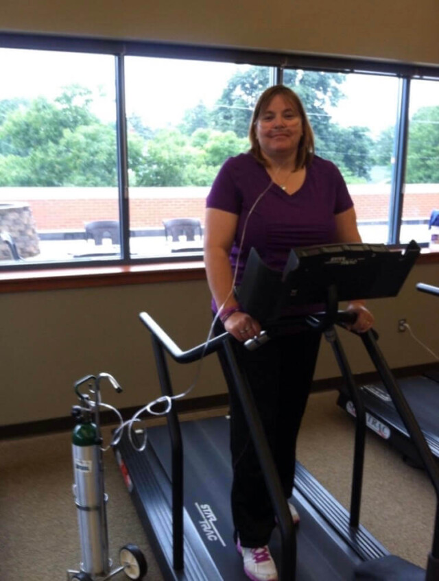 Woman on the treadmill at pulmonary rehab with an oxygen tank and nasal cannula at her side.