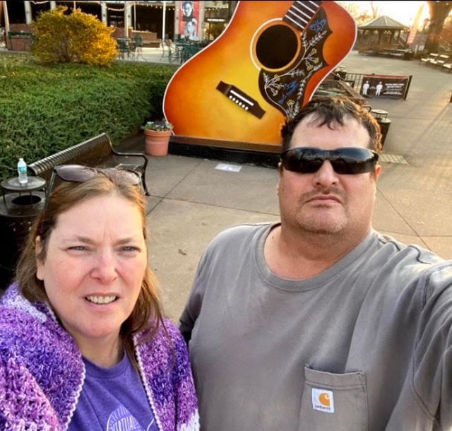 Jackie English and husband standing in front of a giant statue of an acoustic guitar.
