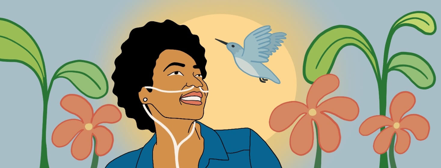 A Black woman wearing oxygen is smiling naturally, looking up at a bird and surrounded by plants and flowers.